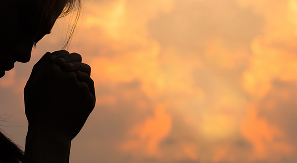 Silouetted image of a head leaning into clasped hands with an orange and yellow cloud filled background